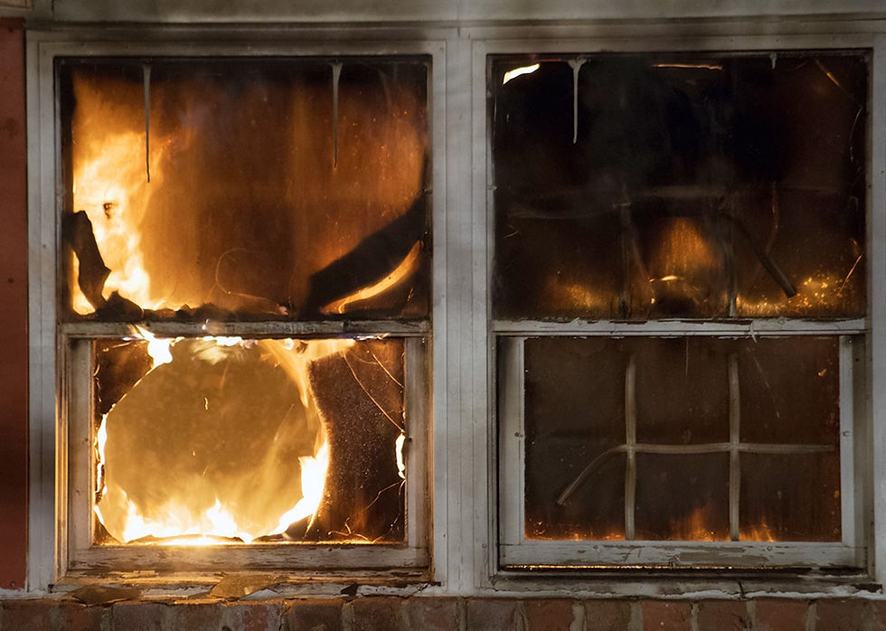 Fire engulfs a room, visible through two windows with broken glass. Bright flames create an intense, dangerous atmosphere.