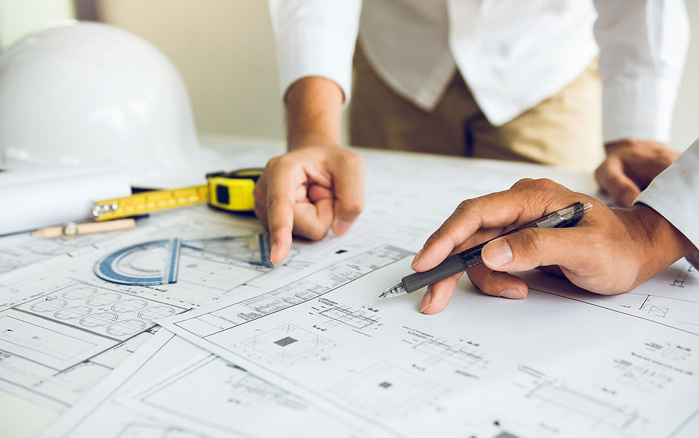 Two people inspect architectural plans on a desk with tools, a hard hat, and a tape measure. Focused and collaborative atmosphere.