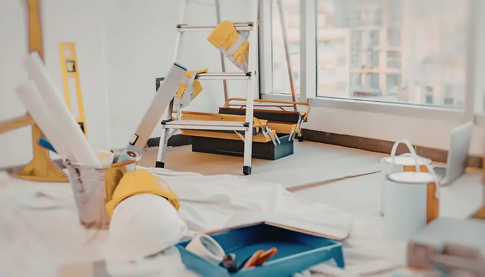 Ladder with tools and paint cans in a bright room under renovation. White sheets cover the floor with a hard hat and level nearby.