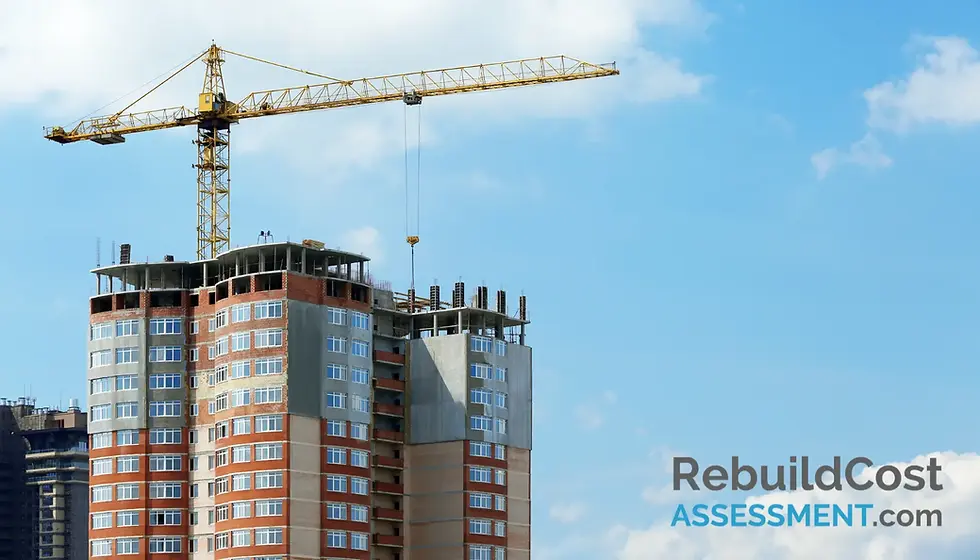 Yellow crane atop a partly constructed high-rise against a blue sky. Brick and concrete building with numerous windows.